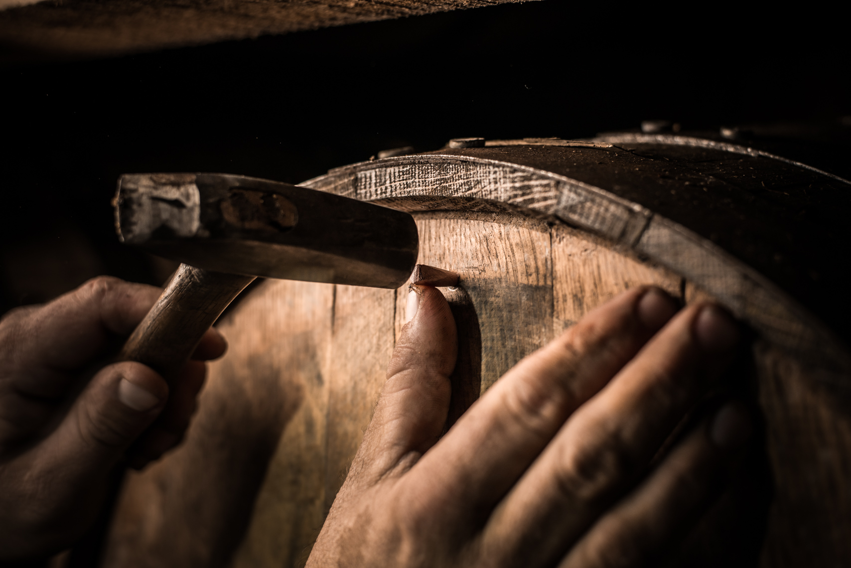 Gritty male hands repair a barrel leak in a warehouse at George Dickel Distillery - Tennessee Whiskey, Reportage, Travel, Narrative, Kentucky, Southern, lifestyle, real life, real people, at work, working, stock photography, reportage, Kristina Krug Photographer, Southeast, Chicago, barrels, bourbon, whisky, photojournalist, photojournalism, Travel Photographer, beverage, industrial, industry, agriculture, liquor, lifestyle, beverage photographer, whisky advocate, beer, southern life, whisky, mash, corn, grains, charcoal, filtration, wood, liquor, storyteller, Cascade Springs, Tullahoma, hands, dirt, working, wood, man, strength, dark, rick house, barrel, barrel house, moody, grit, motion, movement, action, hands, dirt