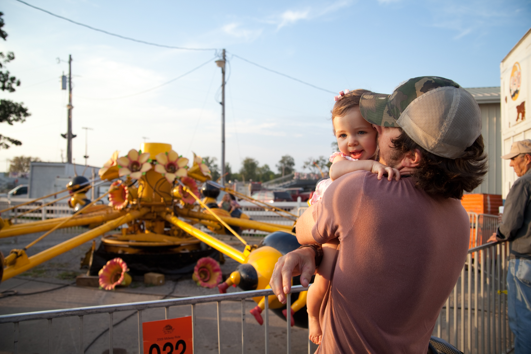 Young father kisses his baby girl on her cheek. Wilson County Fair, Lebanon, Tennessee, carnival, amusement park, rural south, kiss, hug, kissing,Documentary, Editorial, Photojournalist in Nashville, Southeast, South, Texas, Atlanta, New Orleans, Chicago,